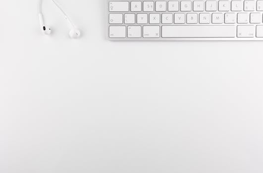 Top view of a white minimalist desk featuring a keyboard and earphones, ideal for technology themes.